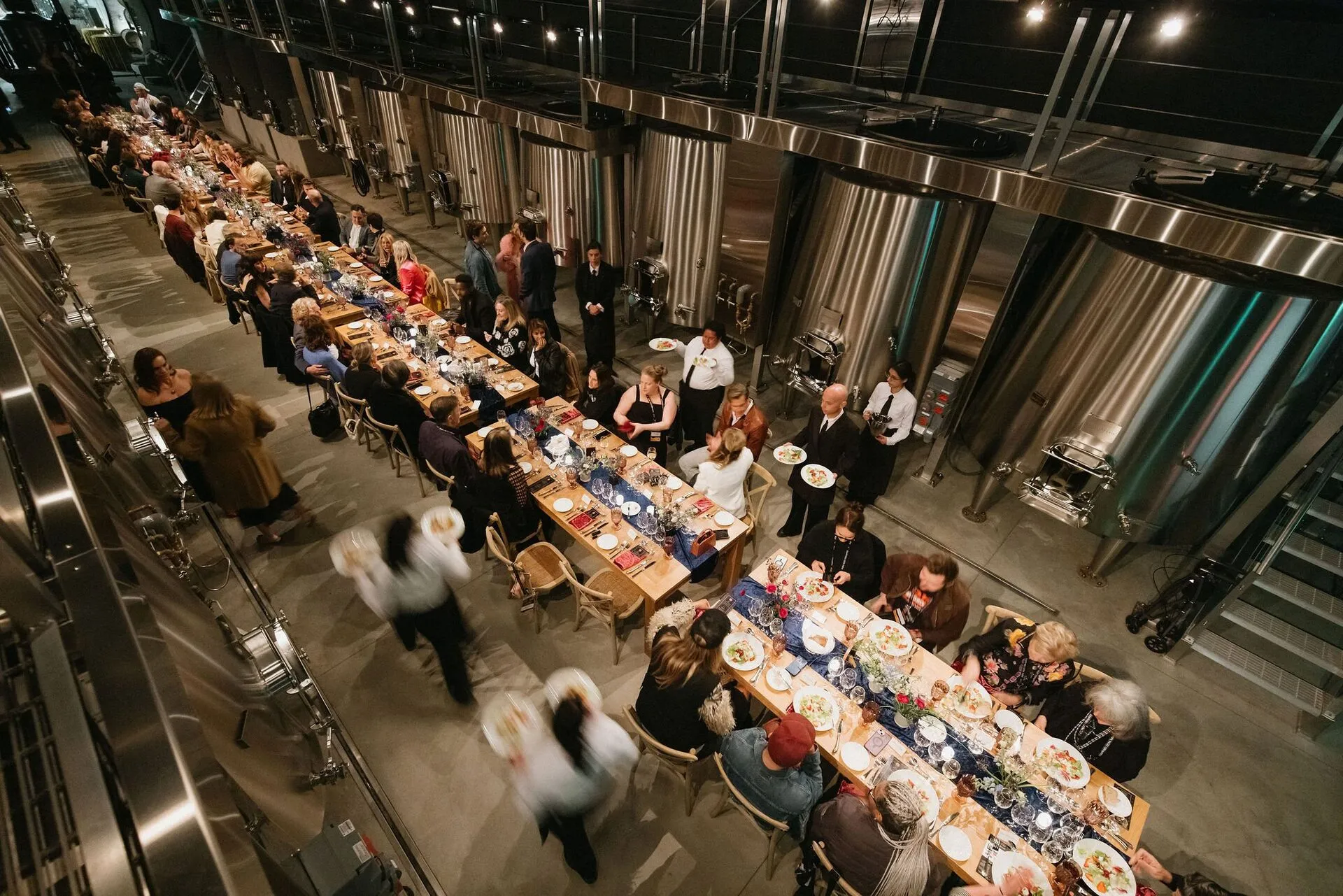Long dining table inside a brewery with guests seated and servers standing